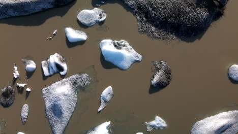 Toma-Aérea-Cenital-De-Muchos-Pedazos-De-Hielo-Rotos-De-Un-Glaciar-En-Agua-Marrón,-En-Islandia,-Heinabergsjökul