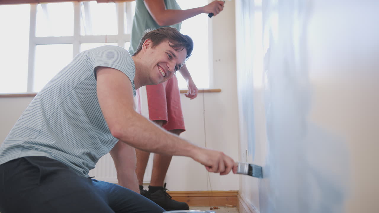 dos hombres decorando una habitación en una nueva casa pintando la pared juntos