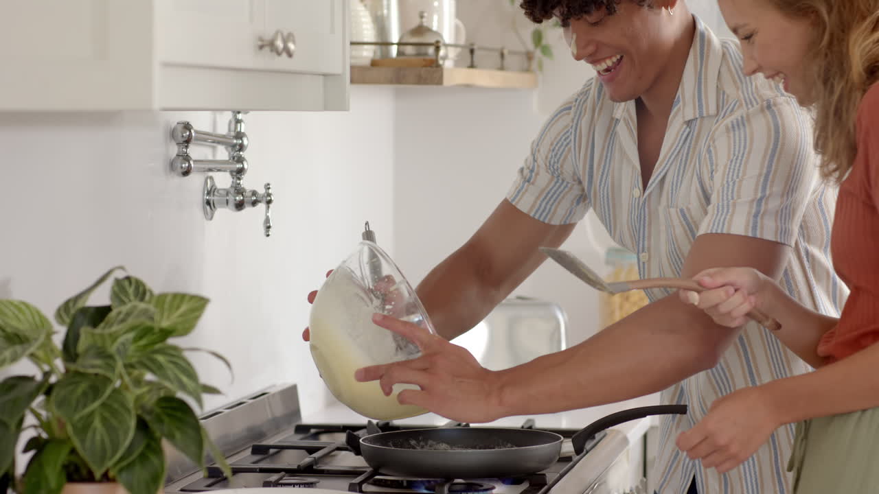 Diverse couple cooking together in kitchen, mixing ingredients and enjoying time, at home