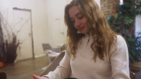 cheerful girl in beige shirt holding coffee cup, smiling while sitting on chair in cozy cafe. relaxed vibe with soft background and natural lighting enhancing inviting atmosphere