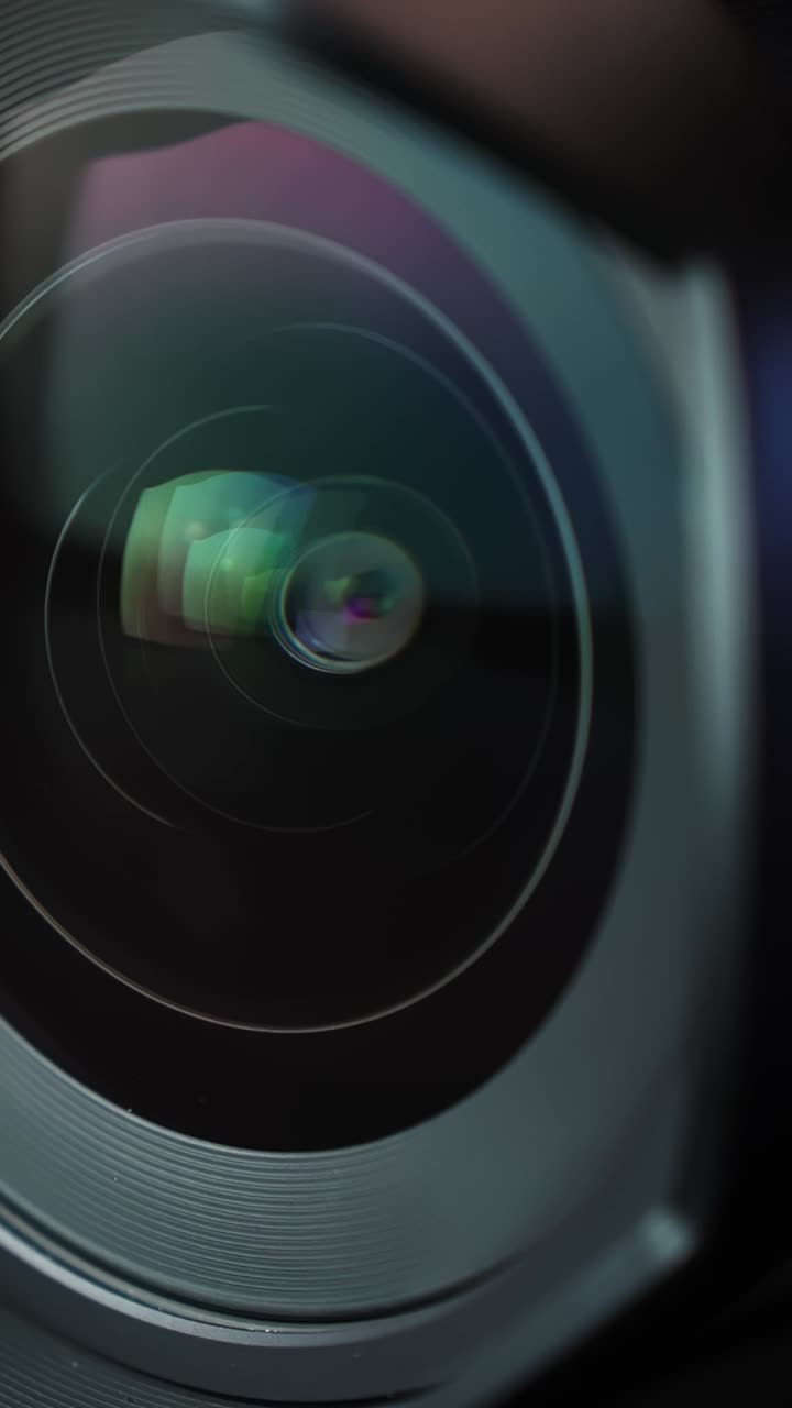 Macro estrema di un obiettivo fotografico mentre le lamelle del diaframma si aprono, rivelando riflessi colorati nel vetro. B-roll tecnologico ideale per fotografia, cinematografia e pubblicità di gadget
