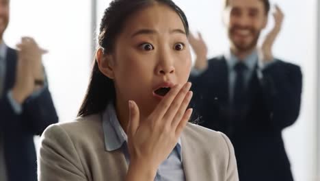 in a contemporary office environment, a woman displays a surprised expression, covering her mouth in shock. a man stands in the background, adding to the unexpected atmosphere.
