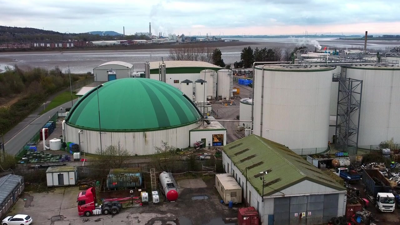 Luftfoto med stigende tilt ned af et industrielt grønkuplet siloanlæg til bionedbrydelig genanvendelse af madaffald.