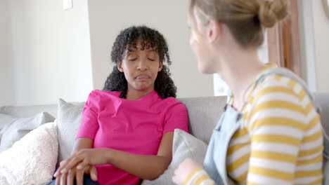 Happy-diverse-teenage-female-friends-talking-and-sitting-on-couch-at-home,-slow-motion