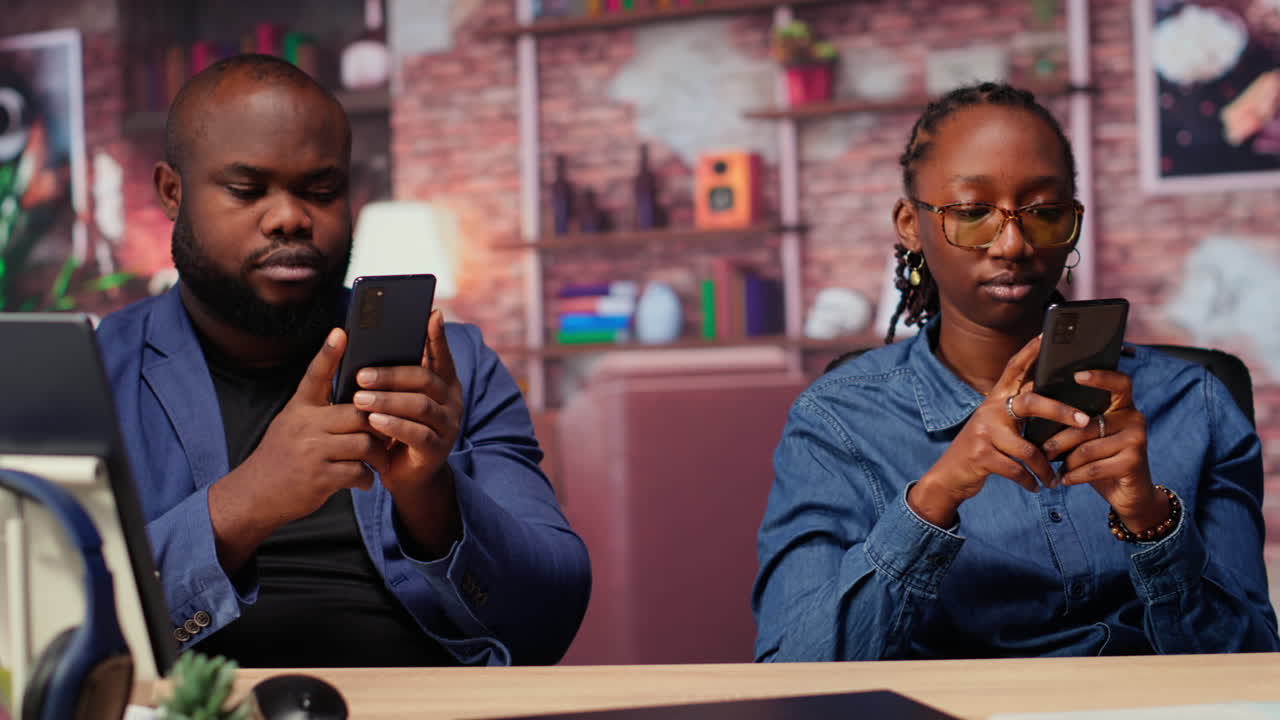 Black couple at home analyzing financial reports on their mobile phones