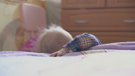 little baby in shirt nibbles plastic tube at bed in room