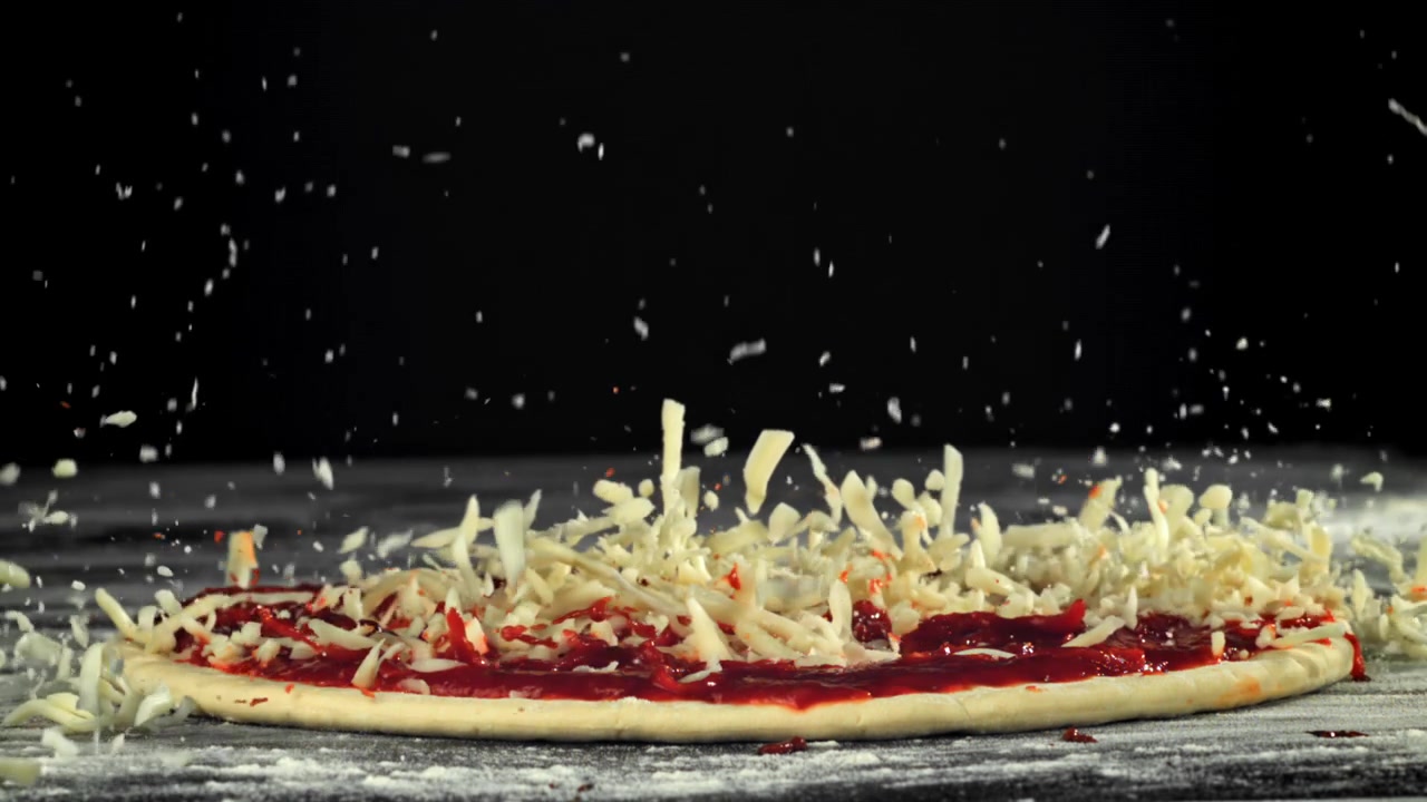 Shredded Cheese Falling onto Pizza Dough with Tomato Sauce in Slow Motion