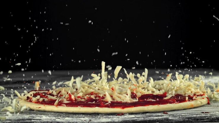 Formaggio sminuzzato che cade sull'impasto della pizza con salsa di pomodoro al rallentatore