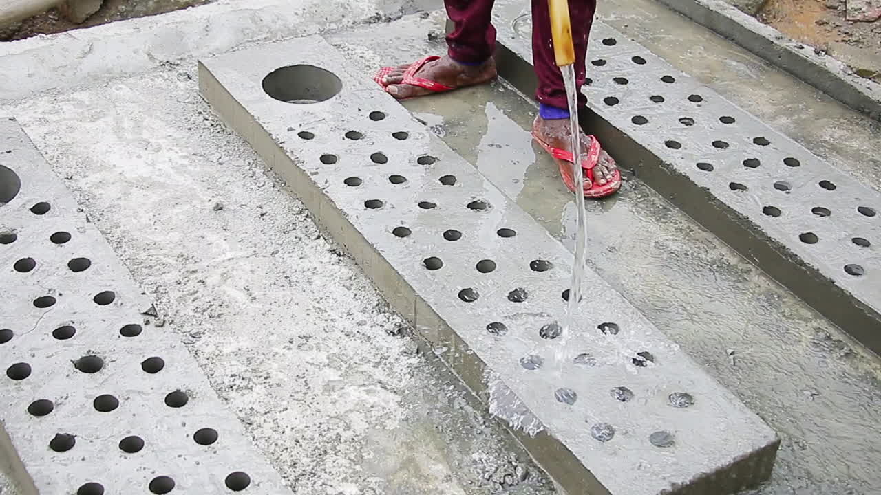 Indian mason worker pouring water on freshly poured concrete slab to increase hardening