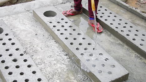 indian mason worker pouring water on freshly poured concrete slab to increase hardening