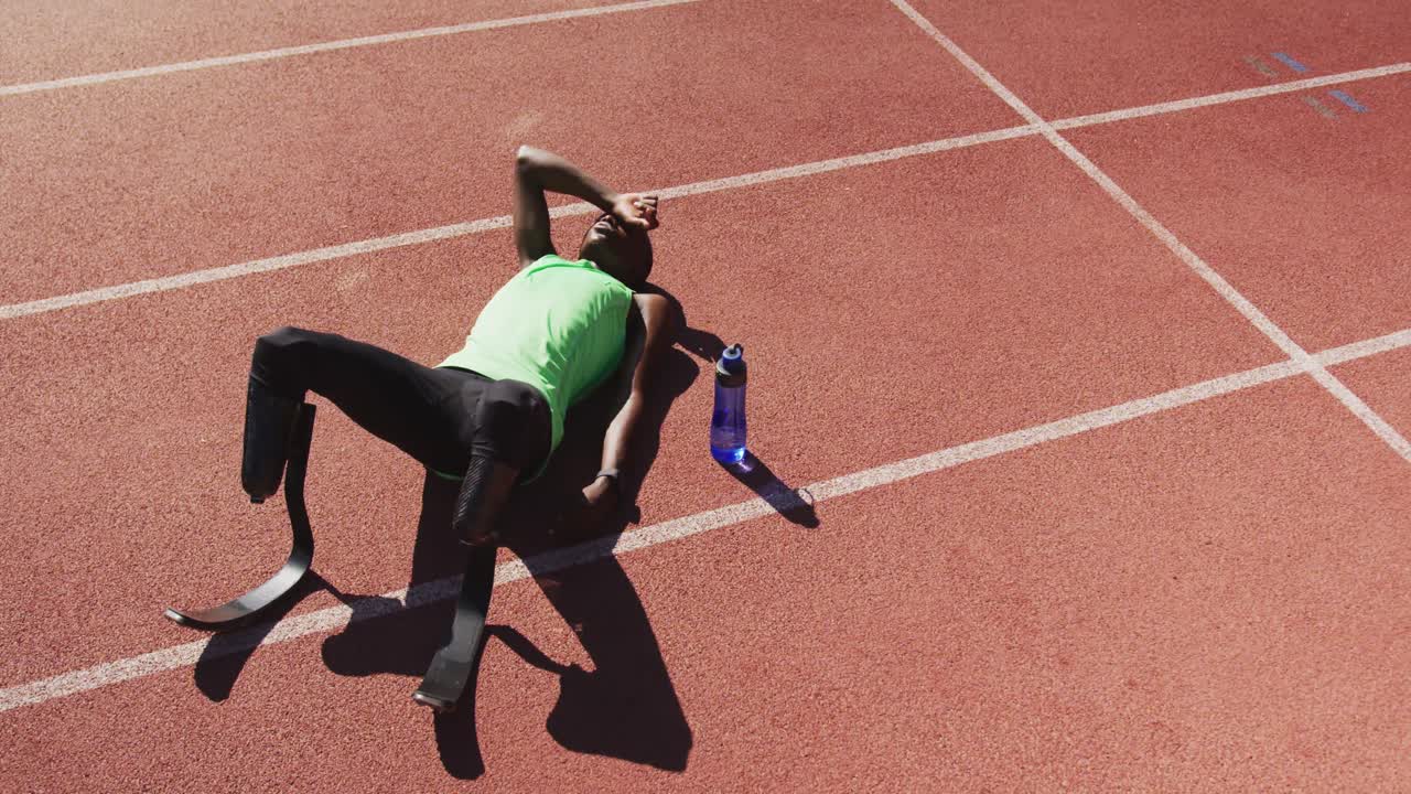 Uomo di etnia mista disabile con gambe protesiche sdraiato sulla pista di atletica.