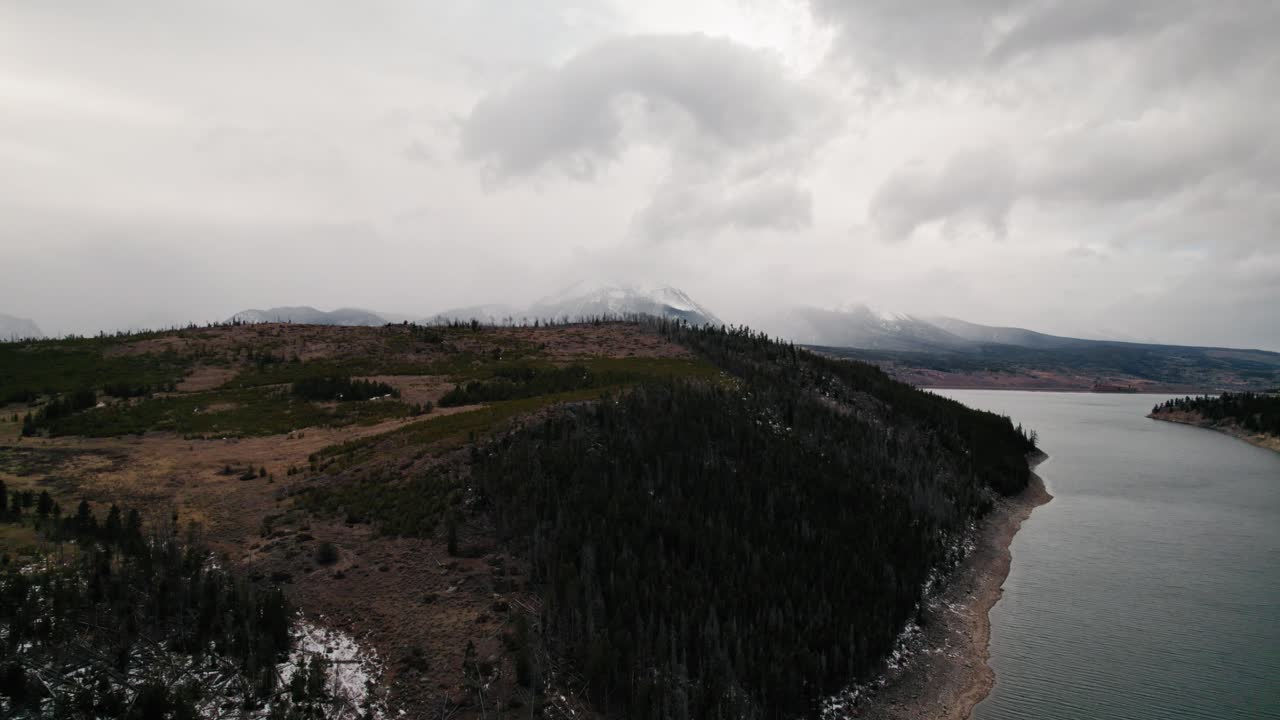 vista aérea de un dron nublado y cambiante que vuela sobre una colina de pinos junto al lago que revela un cuerpo de agua en el embalse de sapphire point dillon, colorado