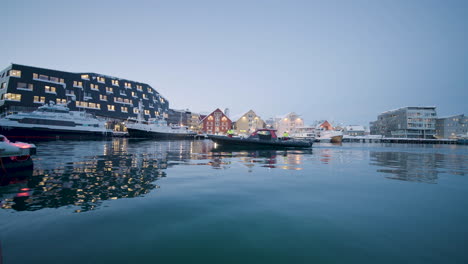 unique and beautiful architecture with boats cruising in calm waters in tromso harbor norway - panning shot