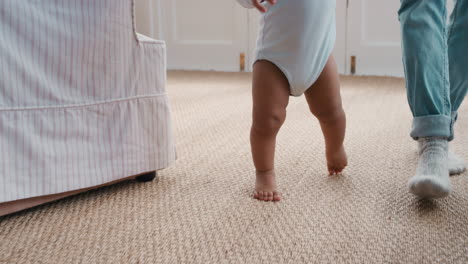 Bebé-Dando-Sus-Primeros-Pasos-Niño-Pequeño-Aprendiendo-A-Caminar-Con-La-Madre-Ayudando-Suavemente-Al-Bebé-Enseñándole-Al-Niño-En-Casa-Confianza-En-La-Maternidad