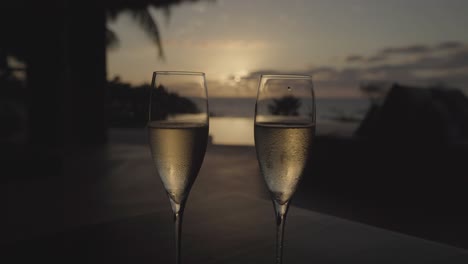 Timelapse-of-chilled-champagne-glasses-at-luxury-resort-villa-with-an-infinity-pool,-ocean-and-sunset-down-the-middle-in-the-background