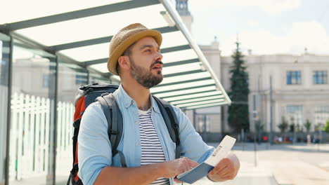 joven y apuesto viajero caucásico con sombrero con mochila viendo pasaporte y boleto en la calle