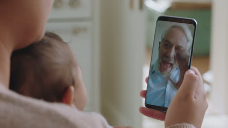 Joven-Madre-Y-Bebé-Teniendo-Video-Chat-Con-Su-Abuelo-Usando-Un-Teléfono-Inteligente-Saludando-A-Su-Nieto-Disfrutando-De-Una-Conexión-Familiar-Charlando-Por-Teléfono-Móvil