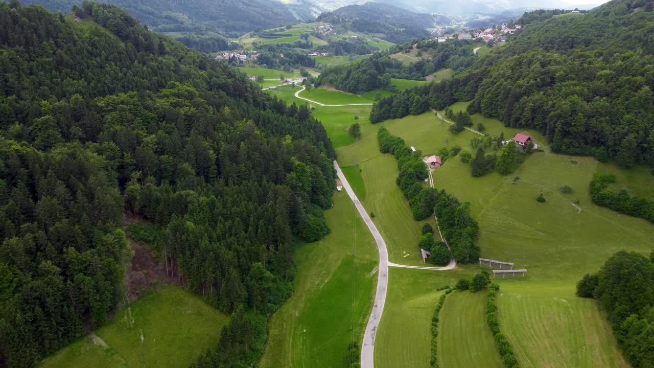 vuelo aéreo lento sobre un camino rural en la zona montañosa verde de eslovenia con bosques profundos, campos verdes y pequeños pueblos