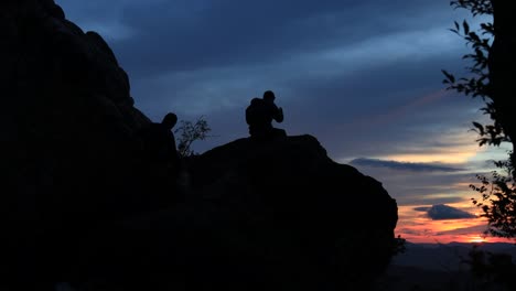 a man sits in silhouette on a large boulder at the dragon's tooth rock monolith on the appalachian trail in virginia and watches the sunrise