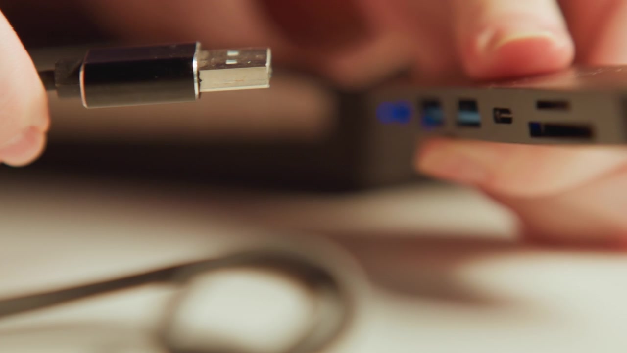 Close angled closeup of hands manipulating black wired earphone 3.5mm jack and cable as connector is aligned with device port on smooth light surface; shallow depth of field isolates fingers