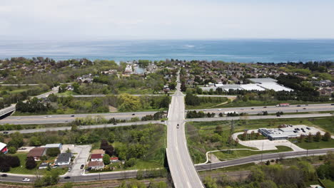 aerial pan shot showing bridge road following over asphalt highway towards lake ontario during summer day