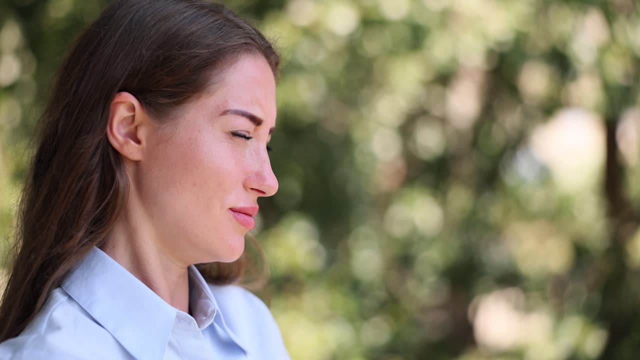 Woman with eyes closed expressing discomfort or pain outdoors