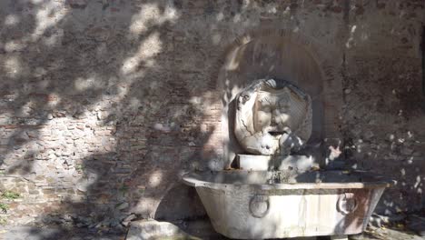 Monumental-fountain-called-Fontana-del-Mascherone-di-Santa-Sabina-located-in-Rome,-slow-motion-with-dolly-forward-move-combined-with-pan-move