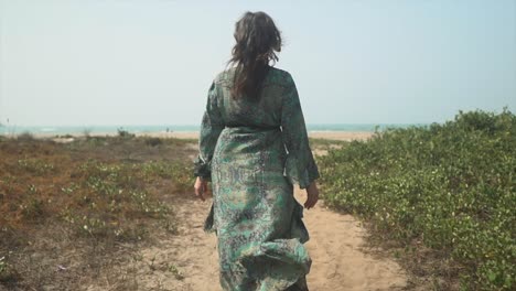 female walking down path towards beach in summer with long flowing dress