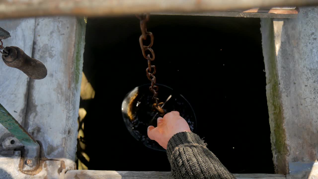 un hombre deja caer una cadena con un cubo en un pozo rústico para sacar agua.