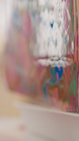 artist takes out sheet covered with abstract patterns in ebru style off tray at small table in studio extreme closeup slow motion. oriental marbling technique