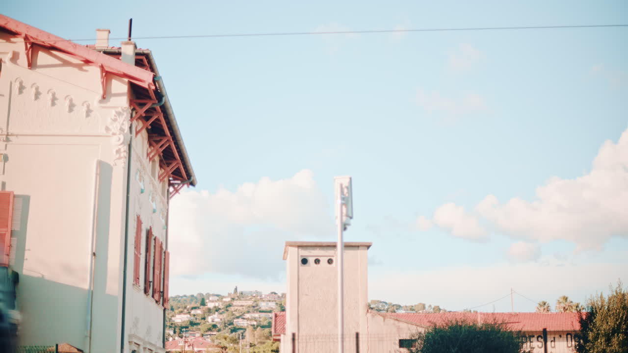 A blue commuter train speeds past a residential building, creating strong motion blur against the still architecture