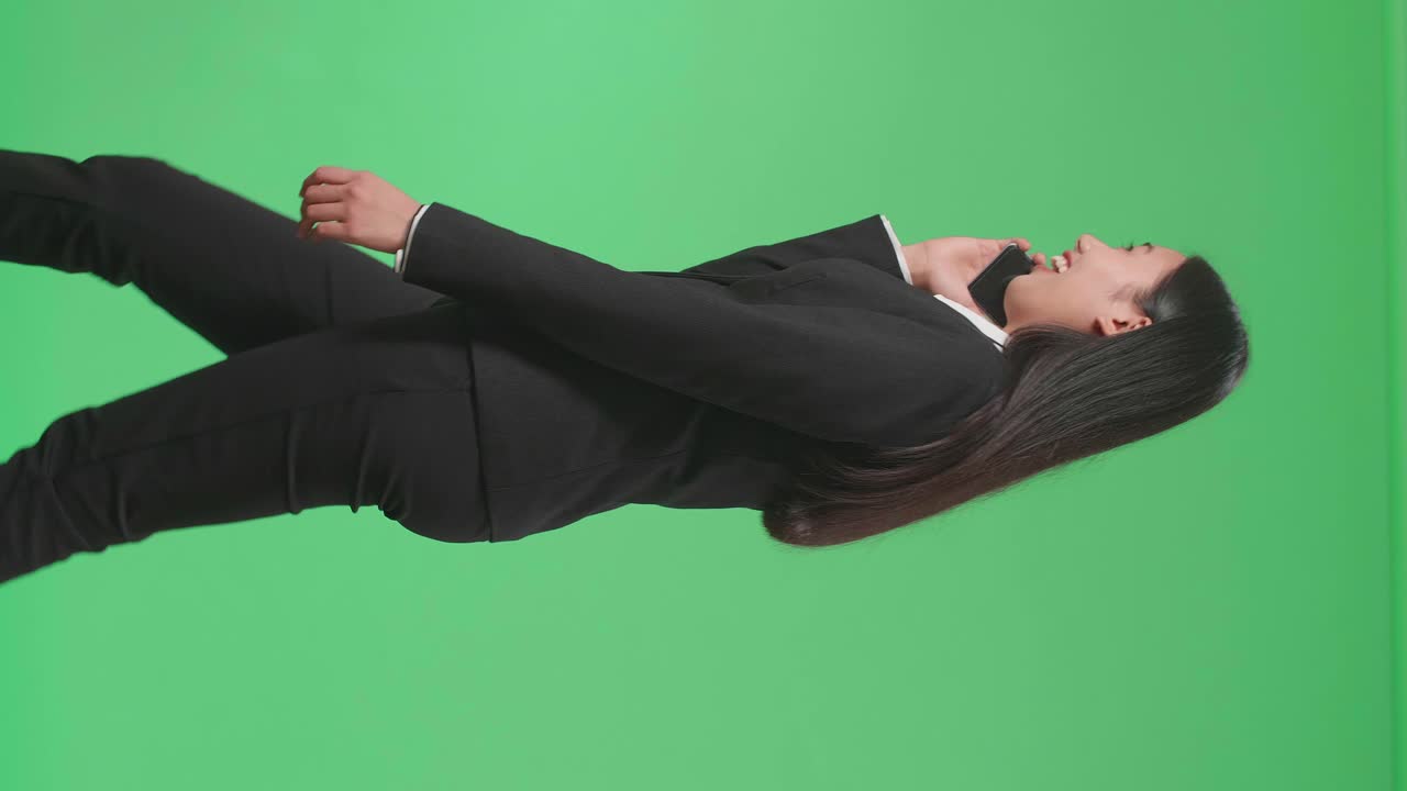 Side View Of A Smiling Asian Business Woman Talking On Mobile Phone While Walking Through Green Screen In The Studio