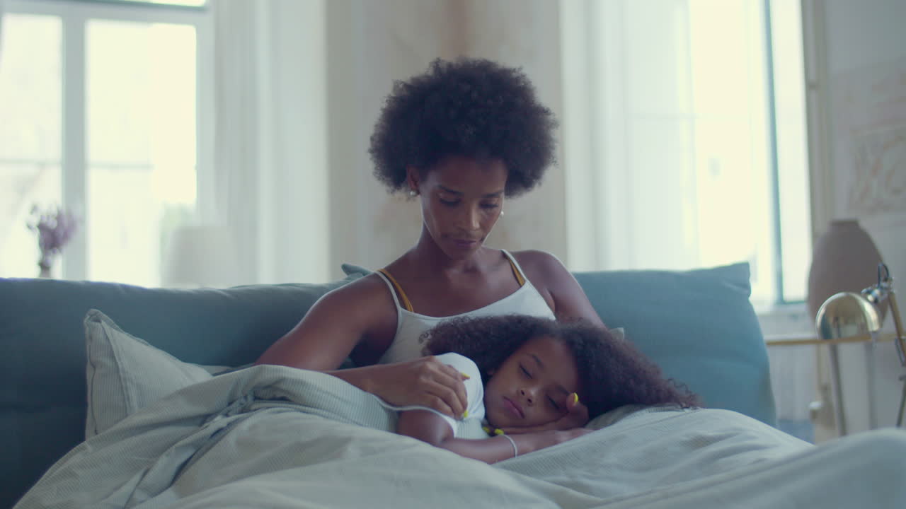 Dolly shot of a caring African American mum stroking her daughter's hair while girl falling asleep