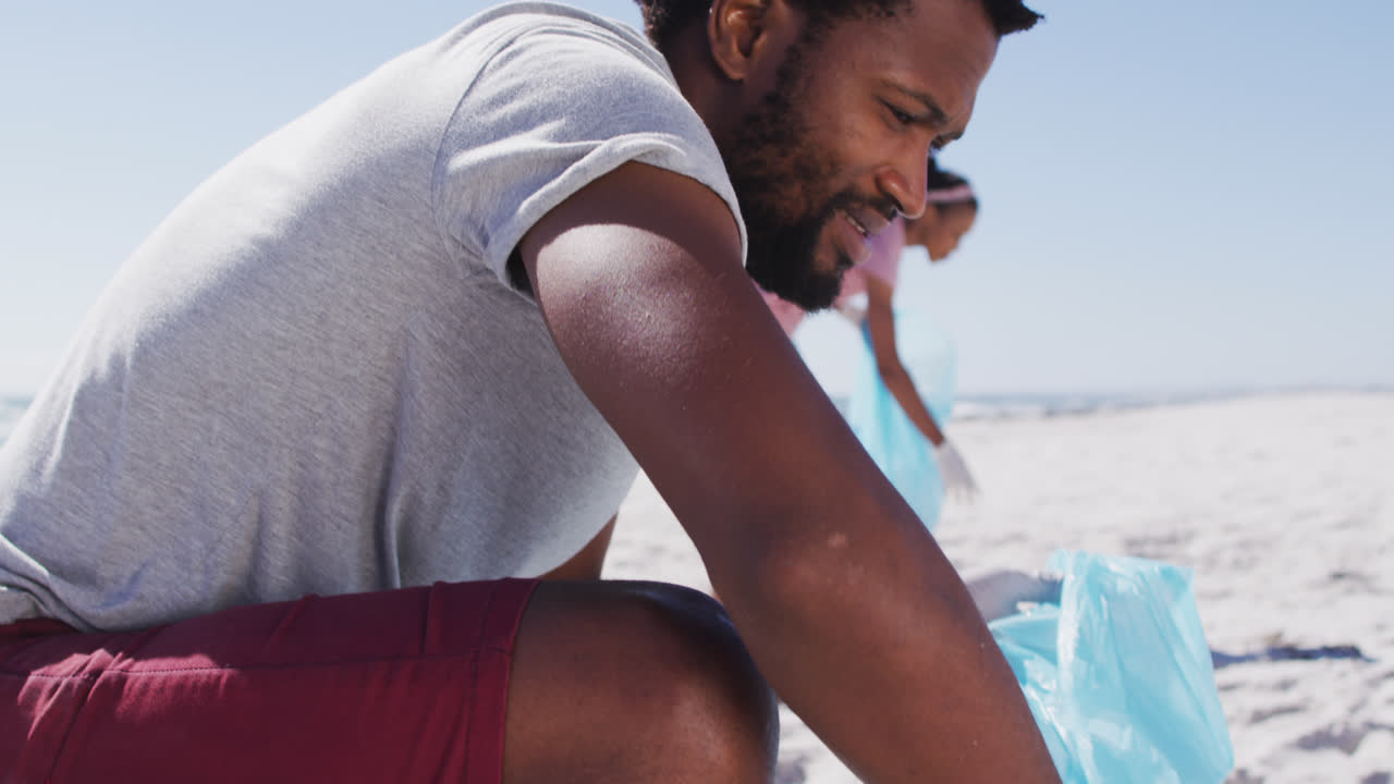 Pareja afroamericana sosteniendo sacos de basura y recogiendo basura de la playa