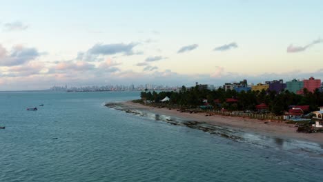 Beautiful-aerial-drone-shot-trucking-left-to-reveal-the-tropical-city-of-Joao-Pessoa-with-a-large-coastline-and-skyscrapers-in-the-distance-behind-a-bunch-of-palm-trees,-located-in-Northern-Brazil