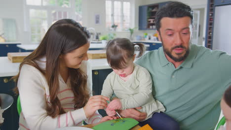 familia con síndrome de down hija sentada alrededor de la mesa en casa haciendo artesanía haciendo tarjetas juntos