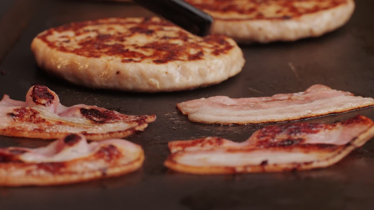 Cooking American fat smash burger and bacon slice on grill close-up. Chiken or fish cutlet smashing by burger press. The chef in kitchen of the restaurant making cutlets for burgers - smash burger beefsteak. Fast and street food concept. High quality 4k footage