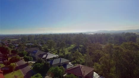 Smooth-aerial-drone-rising-shot-over-suburban-Brisbane,-Australia,-looking-towards-the-Central-Business-District-in-the-distance