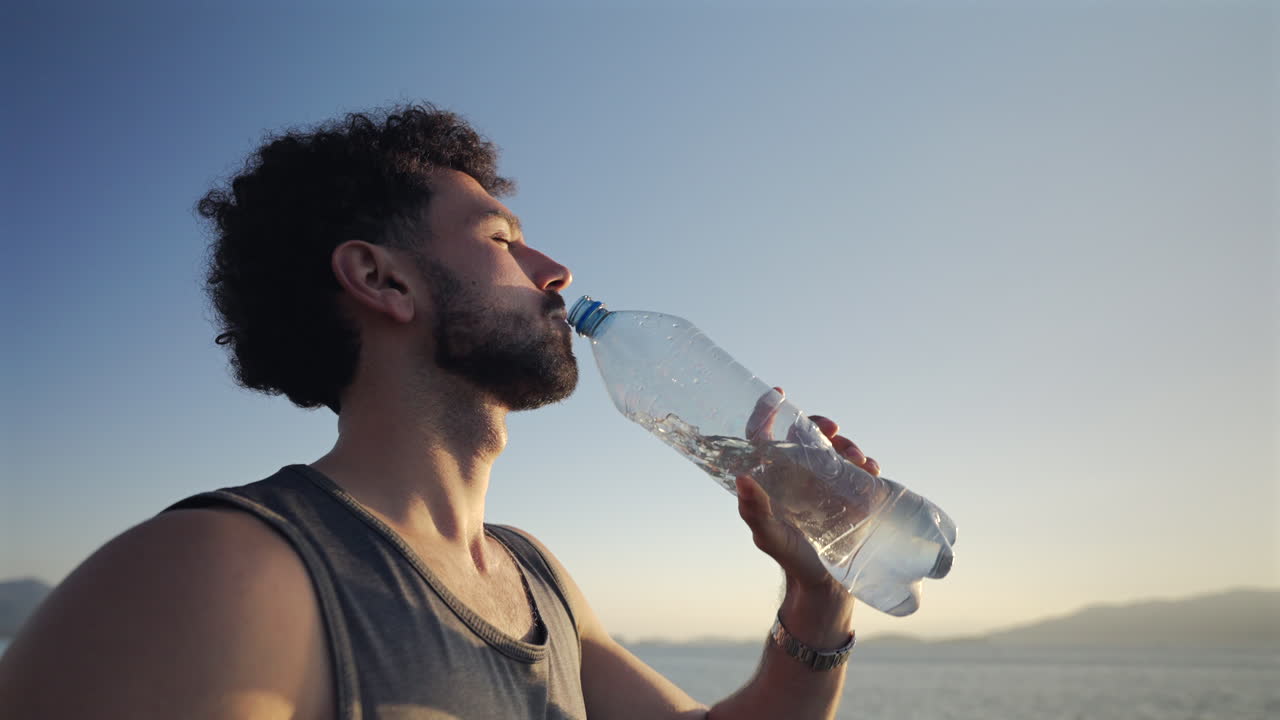 Athlete drinking water during early morning workout on coastal path, fitness lifestyle