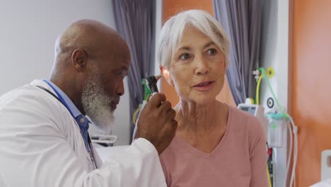 african american male doctor using otoscope examining ear of senior caucasian female patient