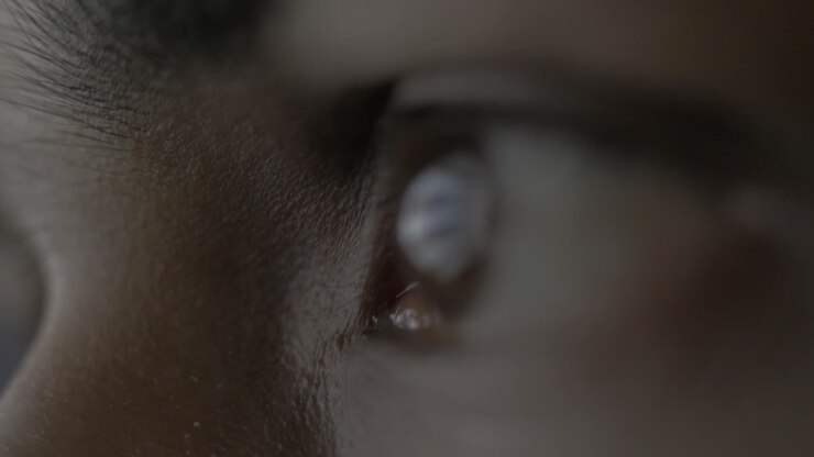 Super extreme close up of a female human eye reflecting a desktop screen while doom scrolling or doom surfing on the web putting unhealthy strain on the eyes