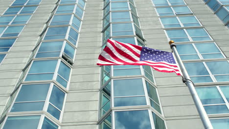 american flag waves in breeze in front of a skyscraper in slow motion