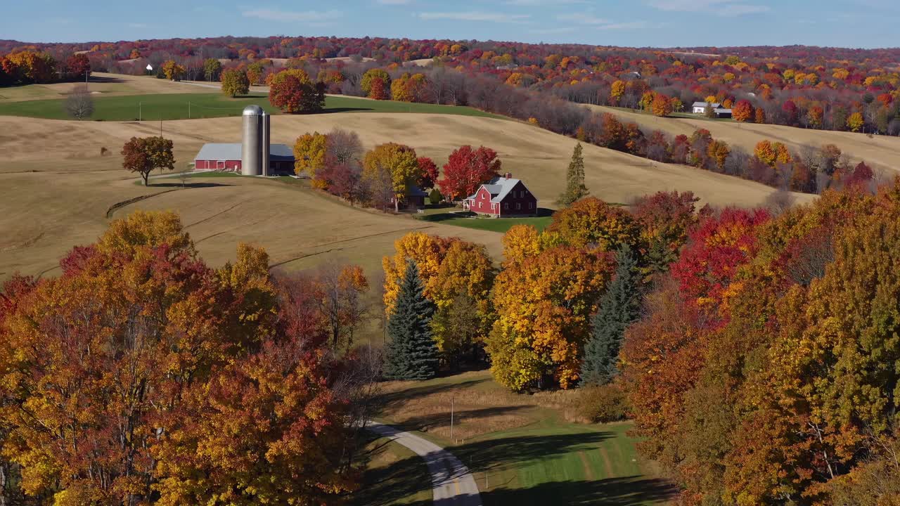 Aerial video captures a picturesque rural landscape in autumn, showcasing vibrant foliage, a red