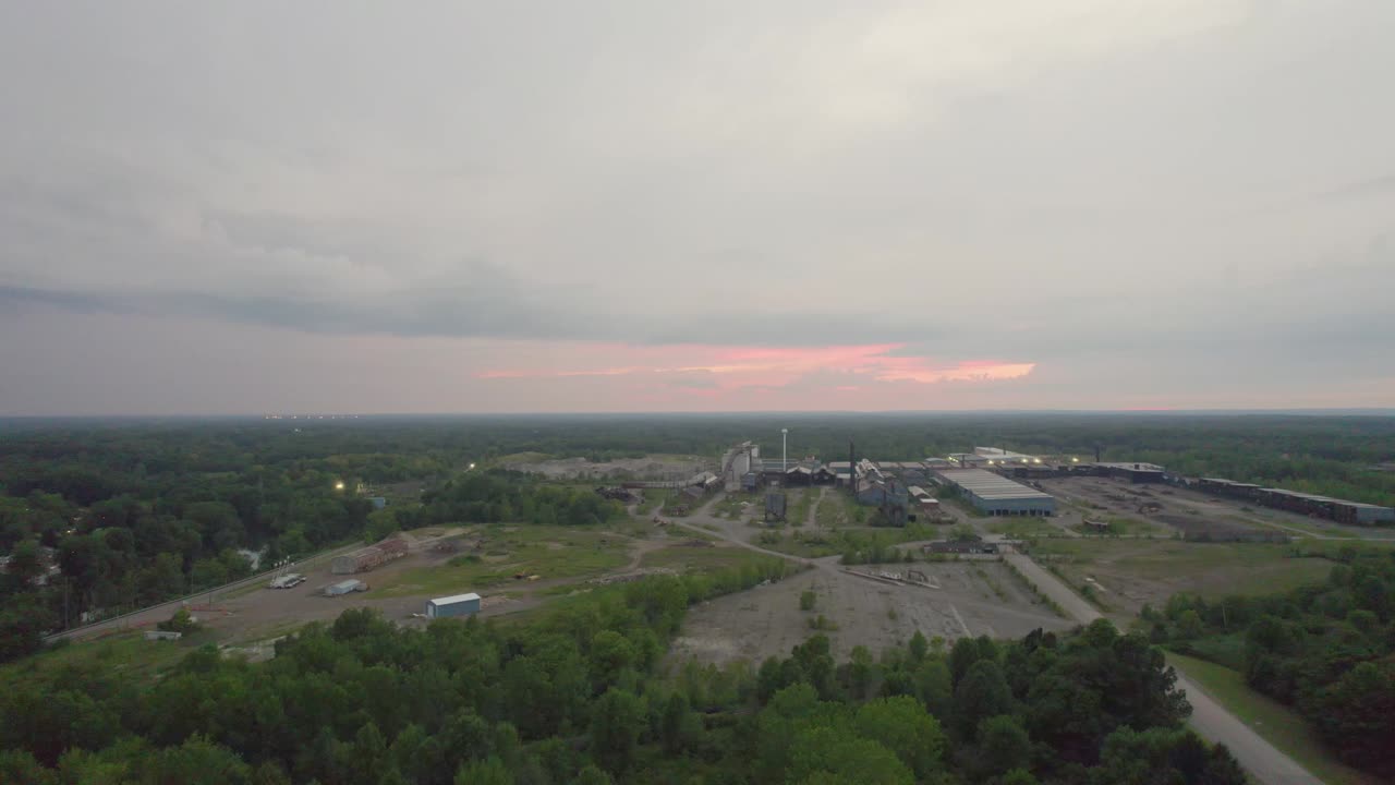 воздушный вид заброшенного промышленного комплекса на закате, демонстрирующий пустынный пейзаж под мягким розовым и оранжевым небом