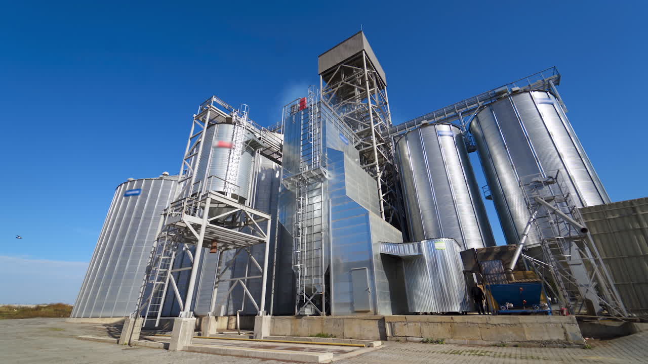 Modern industrial plant. Exterior of a large agricultural complex with silver grain elevators for storage crop. Innovative manufacture in sunny day. Front view.