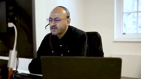south asian businessman wearing headset talking and working at laptop in modern office