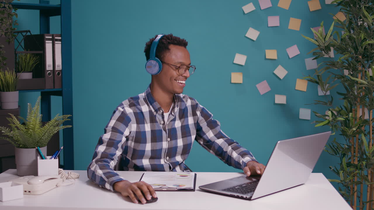 Modern person working on laptop at desk and listening to music
