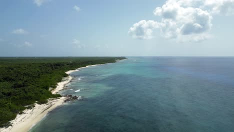 Drone-footage-flying-over-a-turquoise-blue-ocean-and-coral-reef-in-the-Caribbean-with-native-forest-stretching-along-the-beach-into-the-horizon-as-clouds-cast-shadows-over-the-water