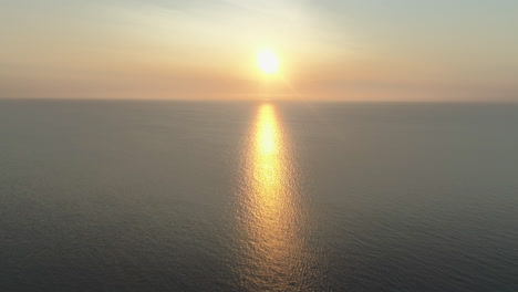 toma aérea de un dron de una hermosa puesta de sol impresionante a la hora dorada sobre el mar hacia el sol con un reflejo asombroso con pequeñas olas y un mar en calma en el reino unido