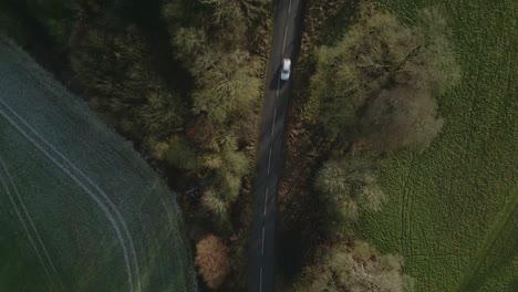 Top-down-aerial-drone-shot-of-an-uk-country-road-in-the-winter-at-sunset-with-cars-passing-by